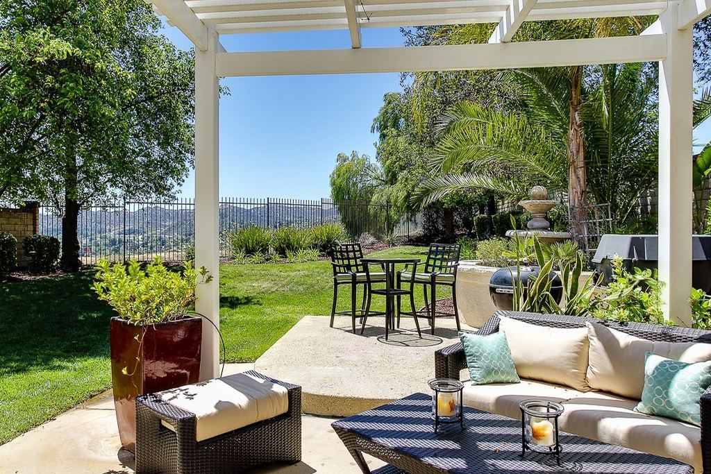 A white pergola shading an outdoor lounge and dining set beside a green lawn