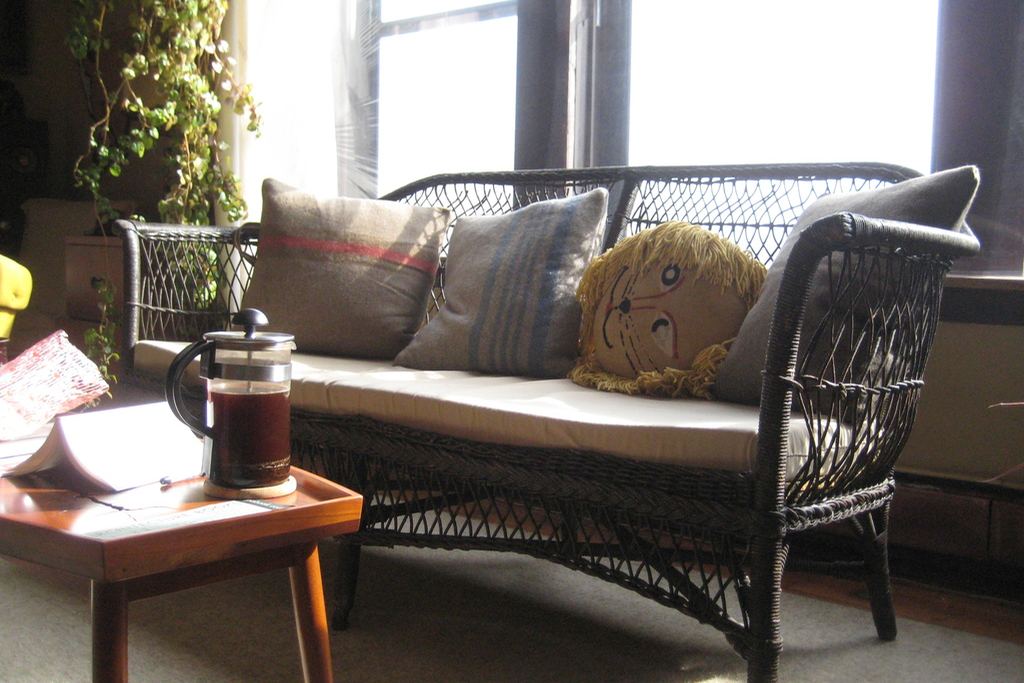 A wicker bench with cushions in front of tall windows filled with daylight
